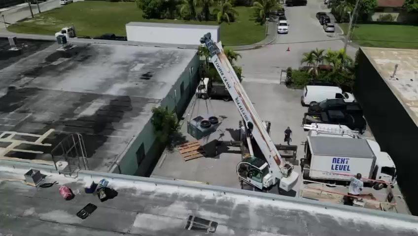 Aerial shot of a crane lifting to a flat roof with the branded box truck in frame