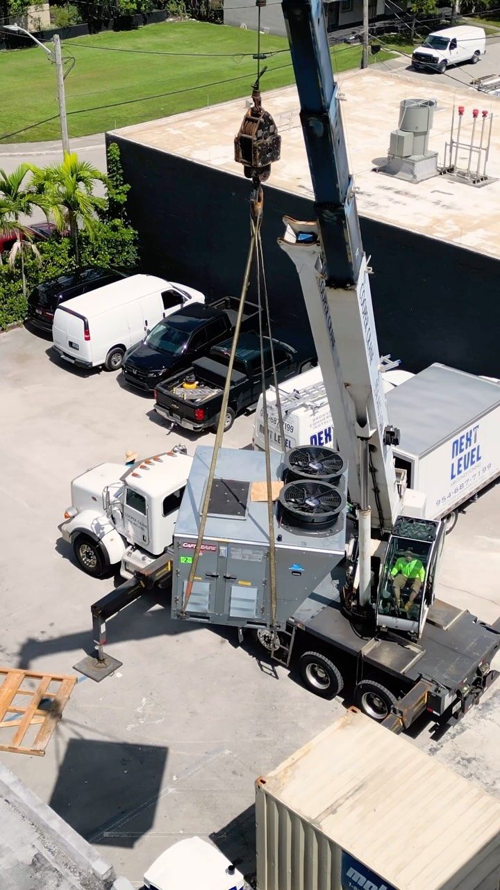 Aerial view of a crane lifting a large custom unit to a roof with the branded box truck below