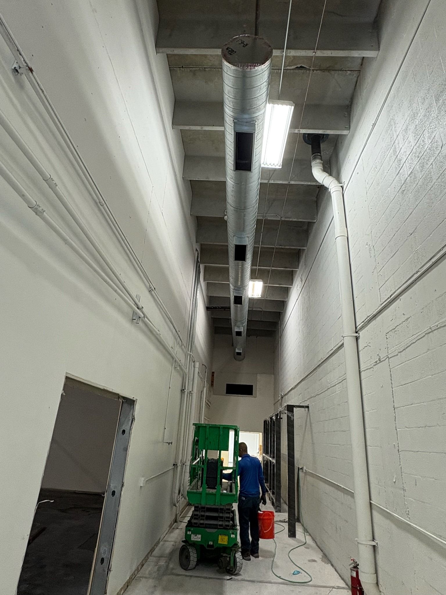 Spiral duct run along a commercial corridor with a technician on a lift, Next Level Air Conditioning job in Boca Raton, 2025