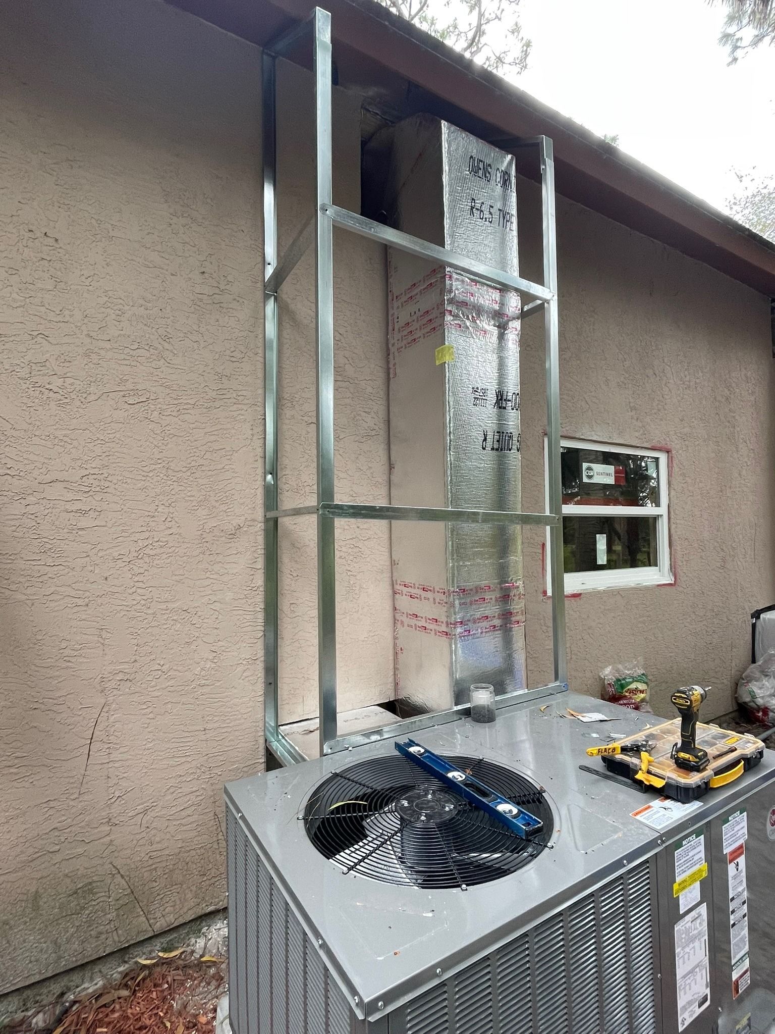 Outdoor unit with a new metal-framed duct chase running up the wall, Next Level Air Conditioning job in Loxahatchee Groves, 2023