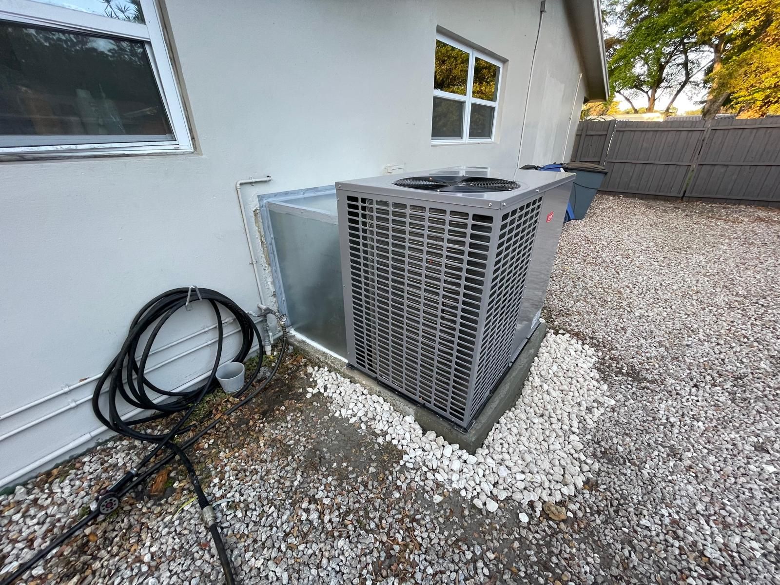 Condenser on gravel beside a house with a fabricated transition plenum