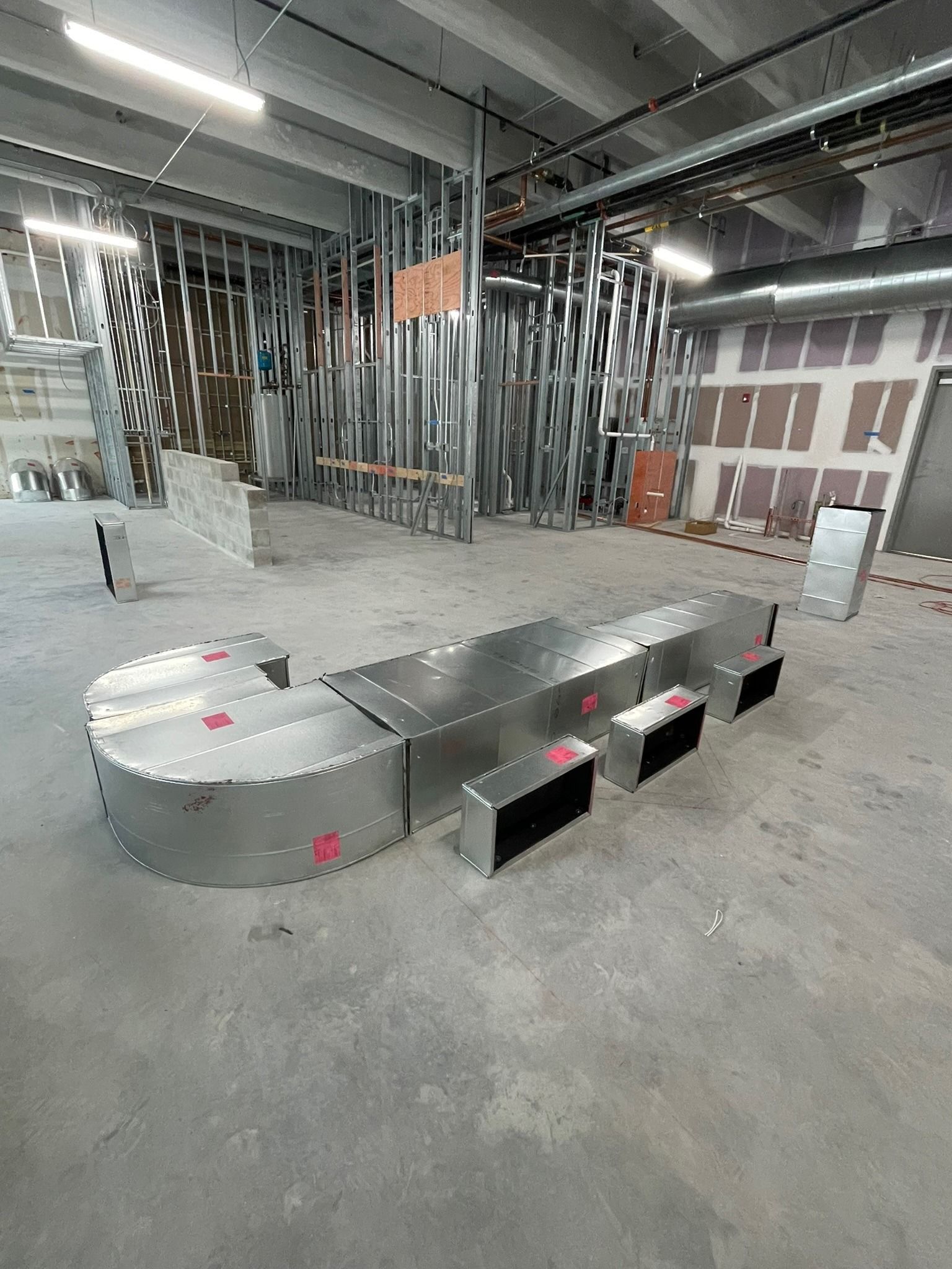 Fabricated sheet metal plenums laid out on the slab of a commercial build-out
