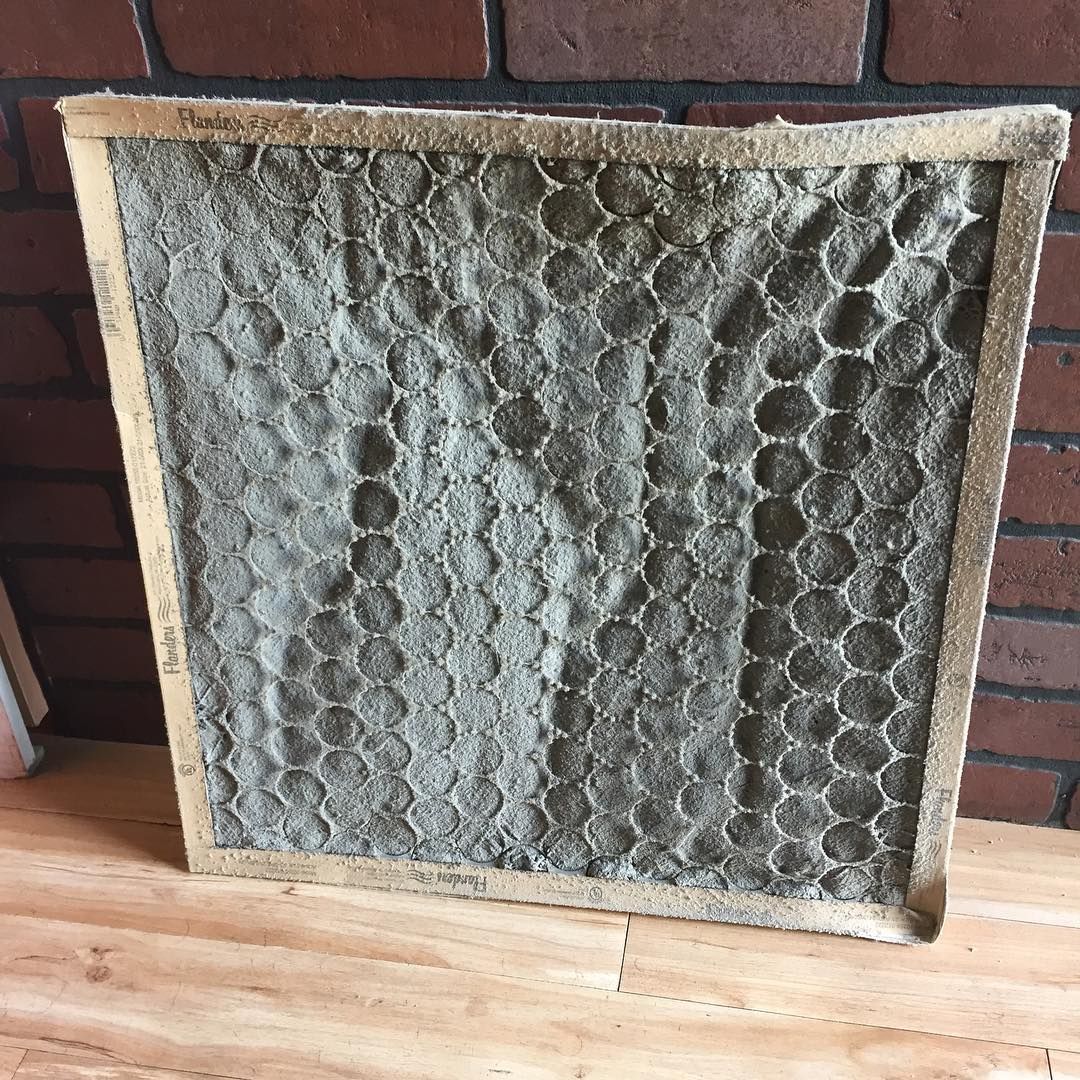 Heavily loaded pleated filter held against a wall, gray with dust