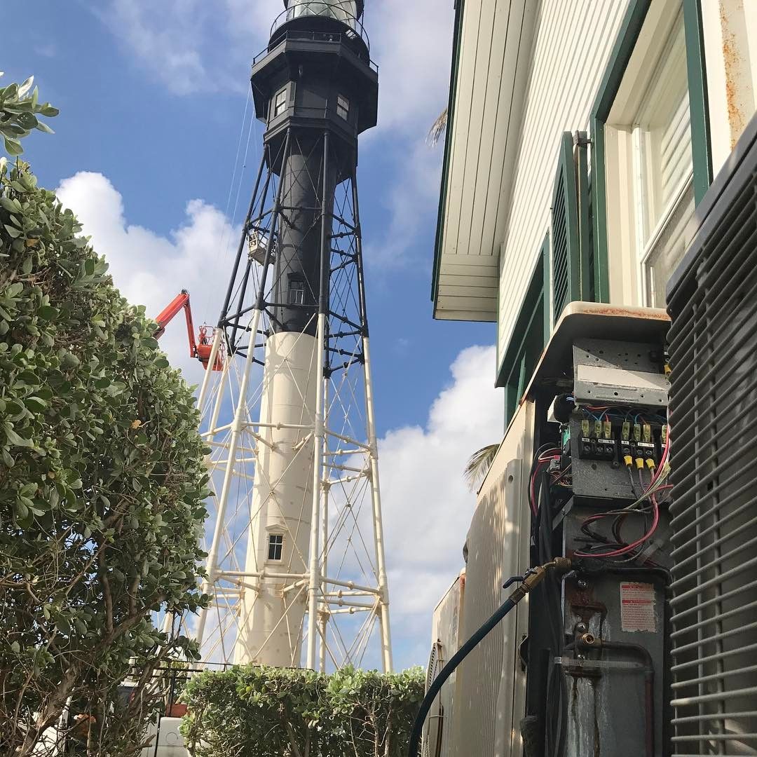 Hillsboro Lighthouse rising behind a condenser with its electrical panel open and gauges connected during a service call