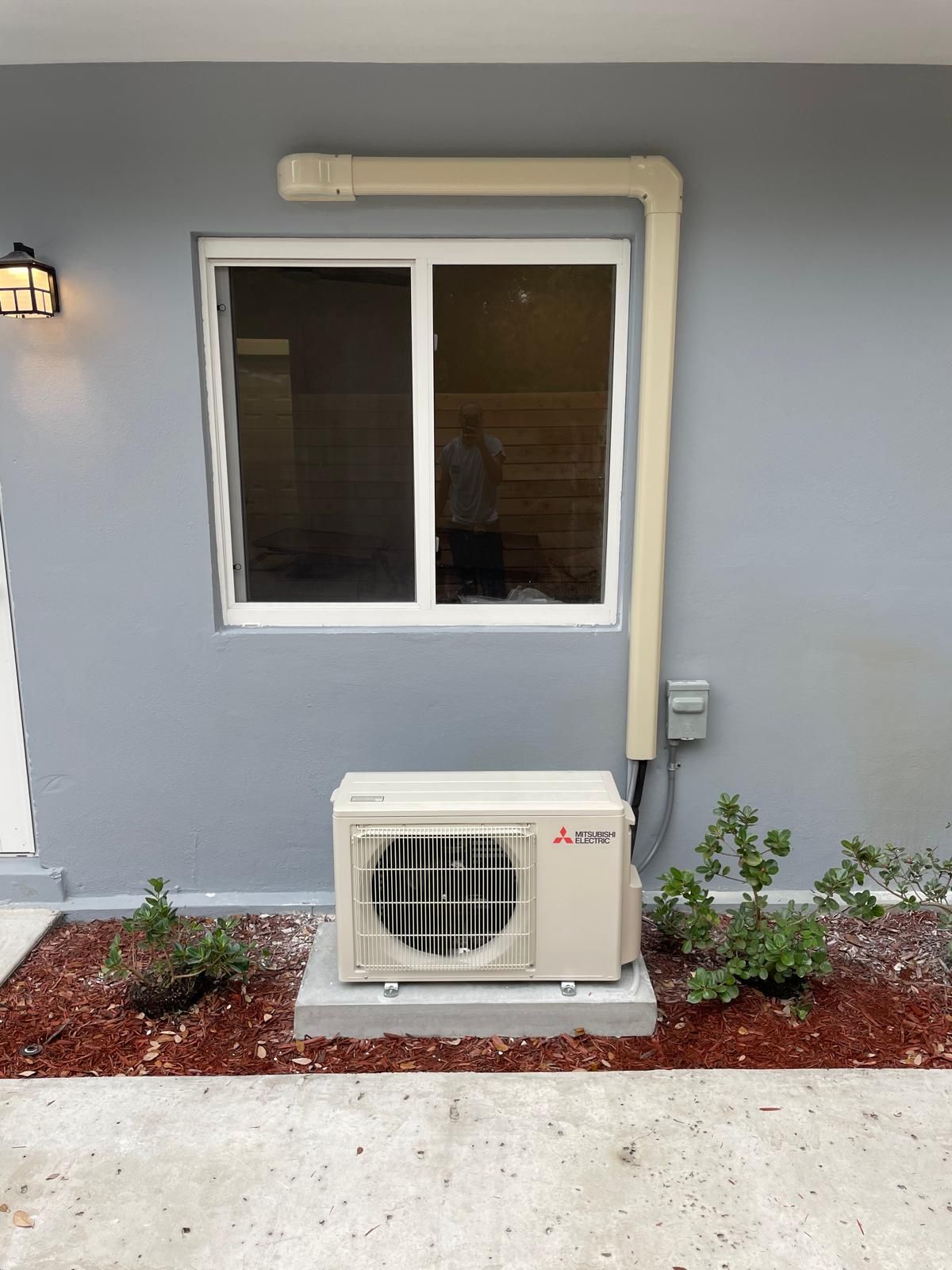Mitsubishi mini-split condenser on a pad against a gray wall, finished install