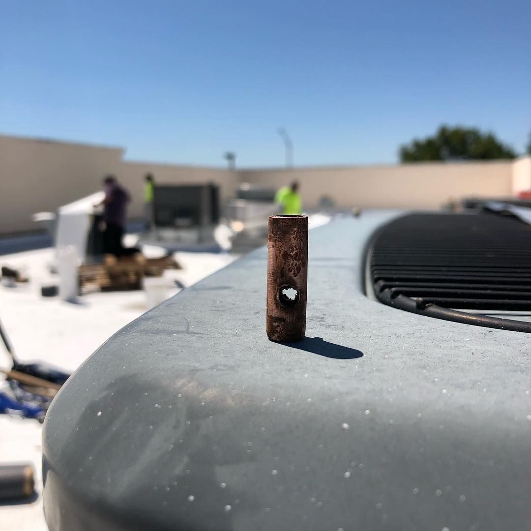 Cut section of copper refrigerant line stood on a rooftop unit with a corrosion pinhole clearly visible