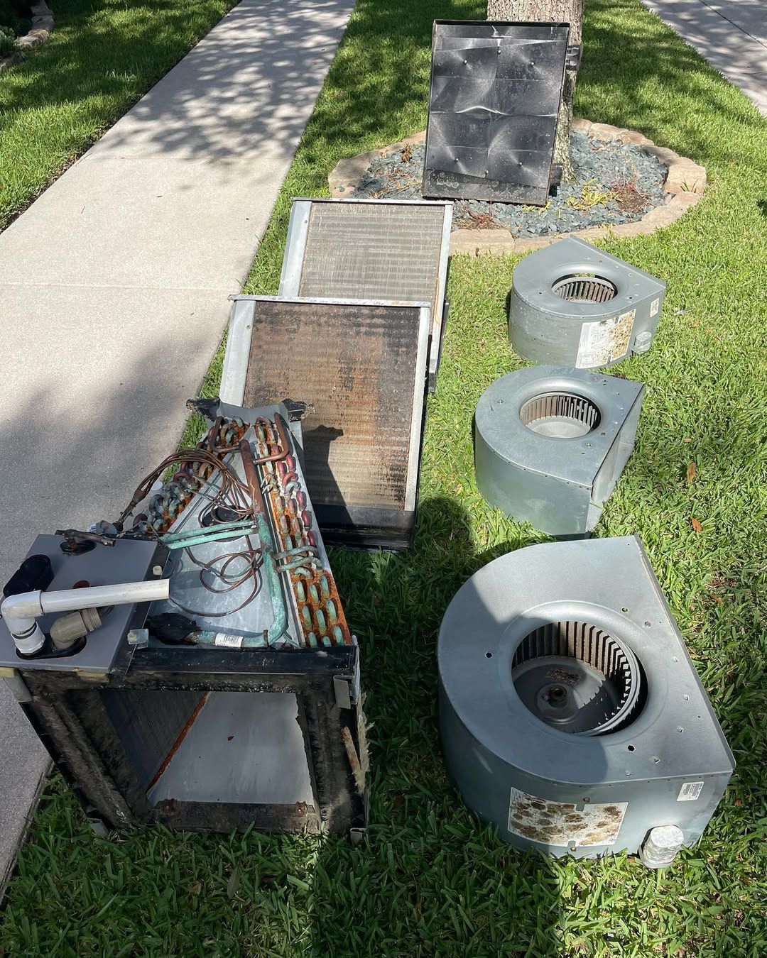 Removed blower assemblies, a corroded evaporator coil and a filthy filter rack laid out on a lawn
