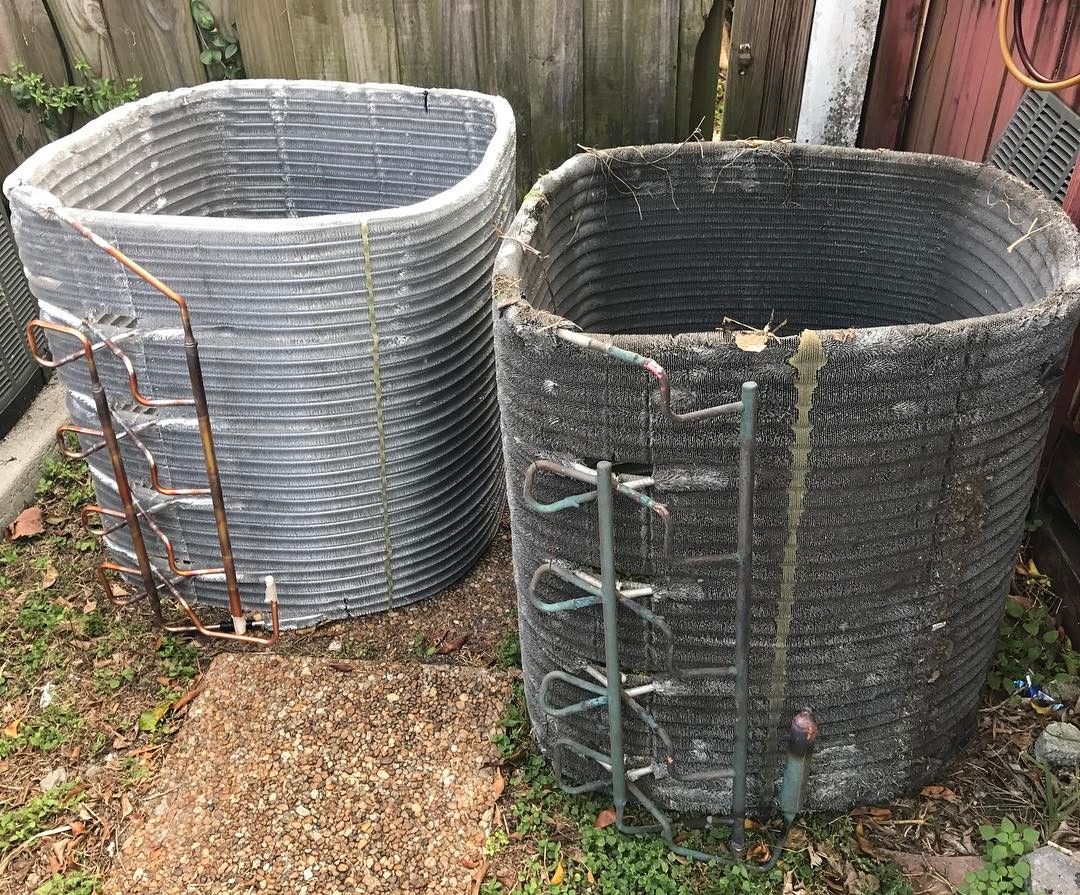 Two removed condenser coils standing in a yard, one cleaned and one still fouled