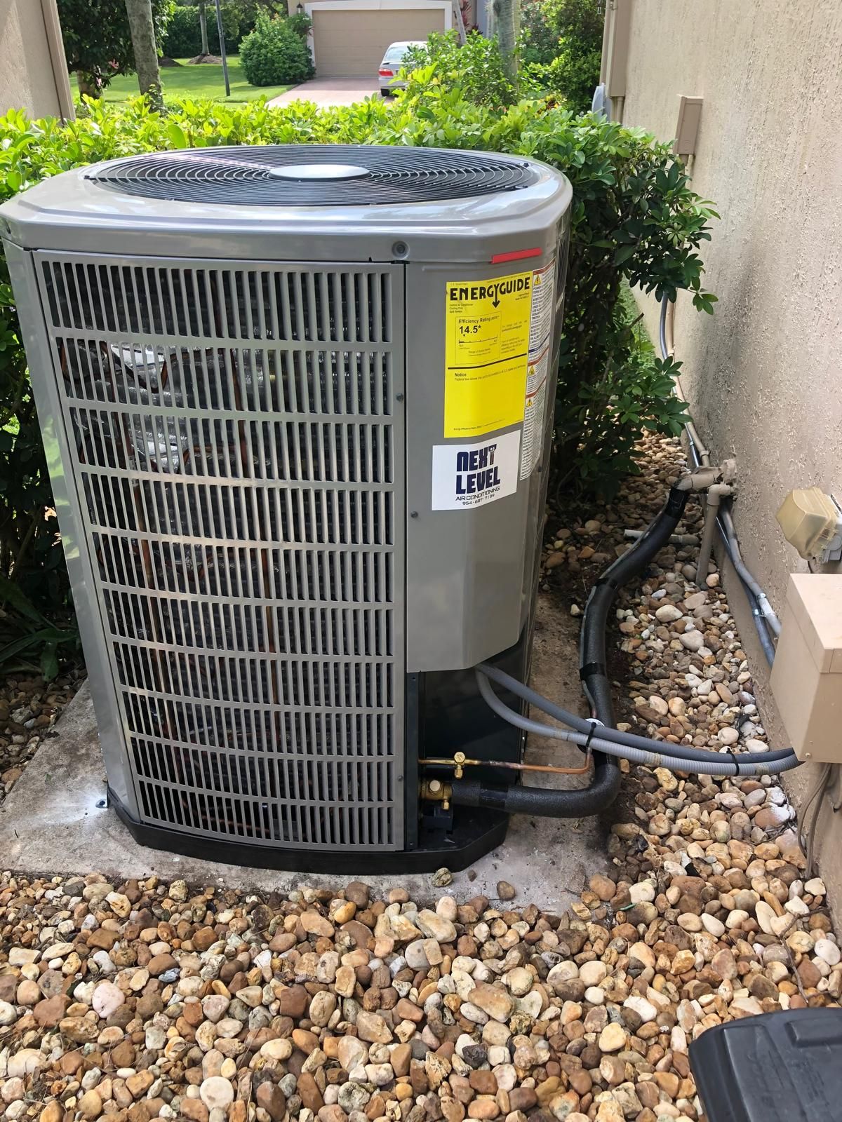 Residential condenser on a pad in a gravel bed with a Next Level sticker on the cabinet