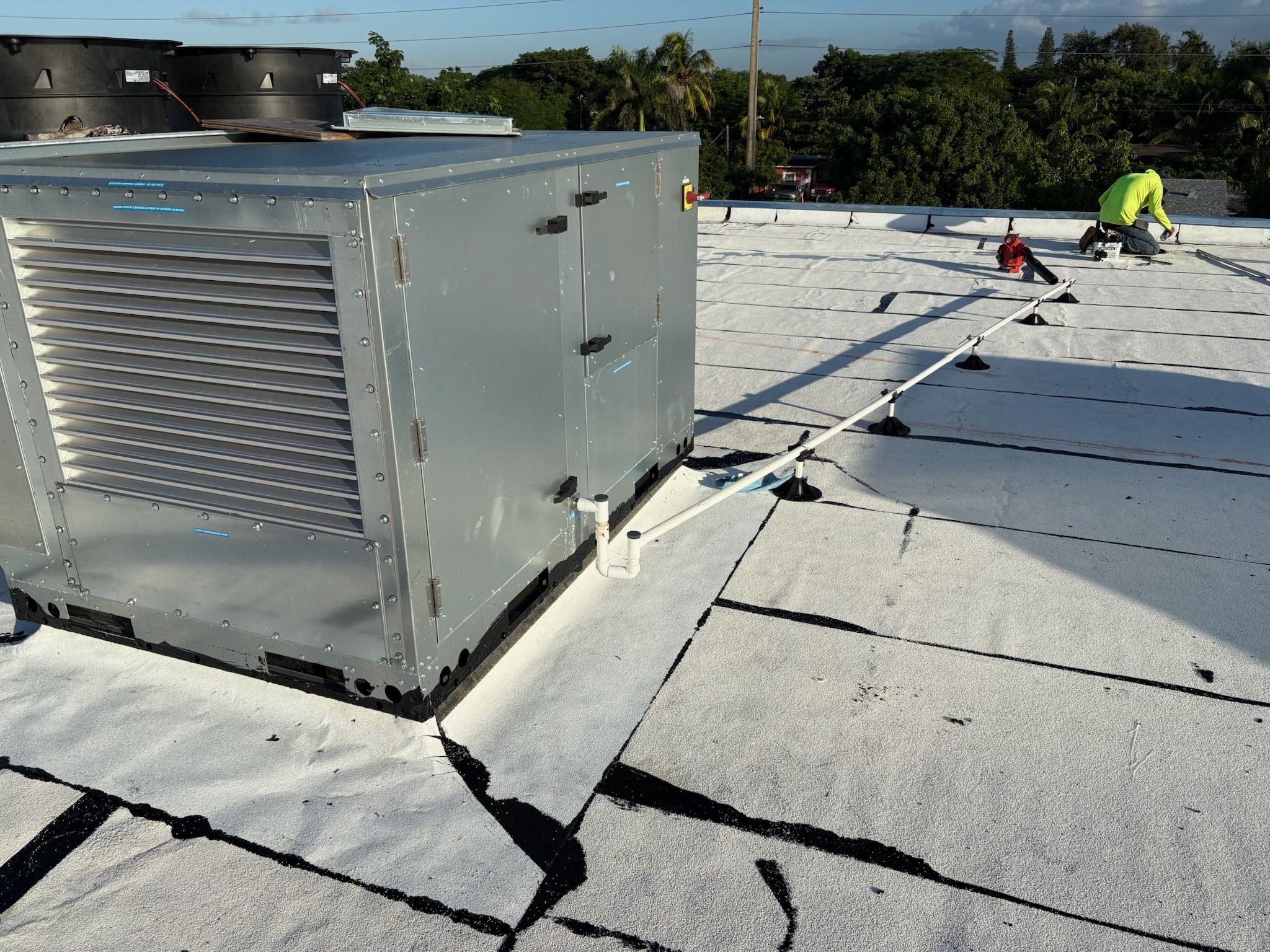 Rooftop package unit on a flat commercial roof with a technician working behind it