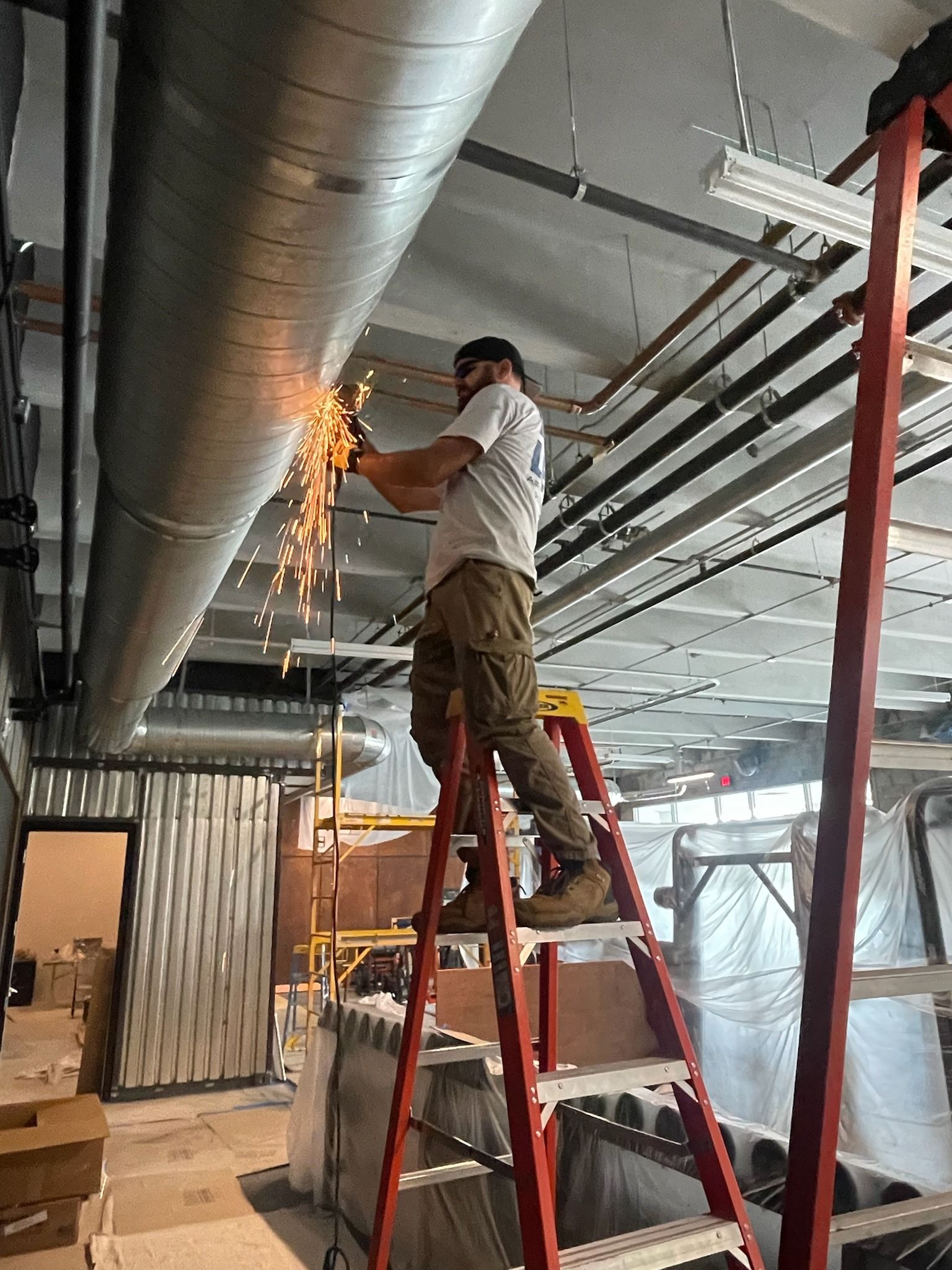 Technician on a ladder cutting spiral duct in a commercial space, Next Level Air Conditioning job in Fort Lauderdale, 2024