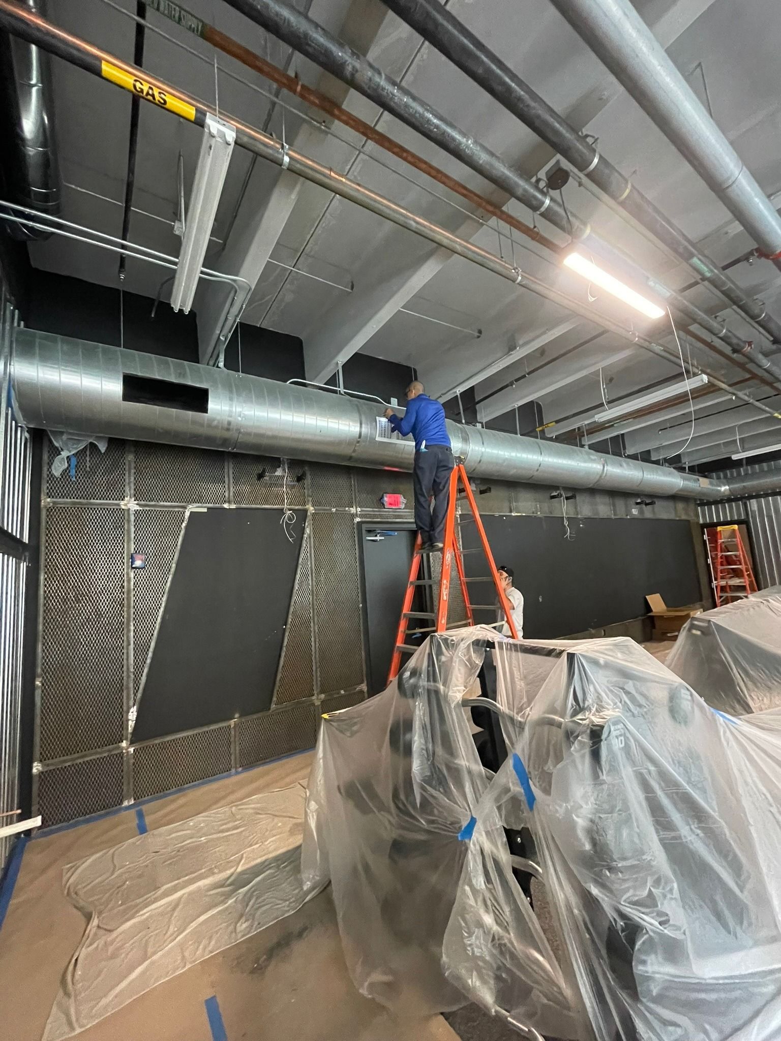 Technician on a ladder hanging spiral duct in a commercial build-out in Fort Lauderdale