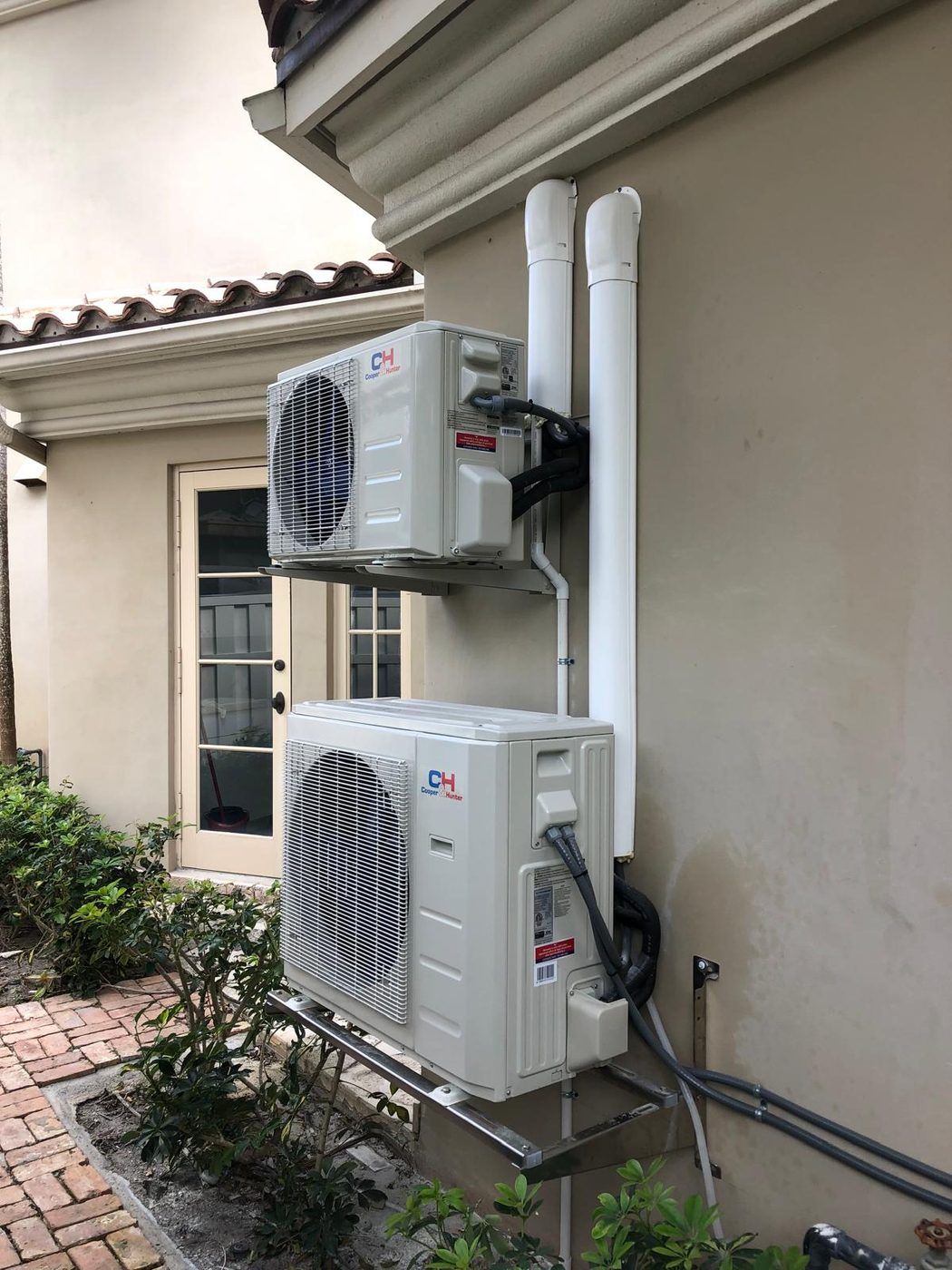 Two Cooper and Hunter mini-split condensers on wall brackets against stucco